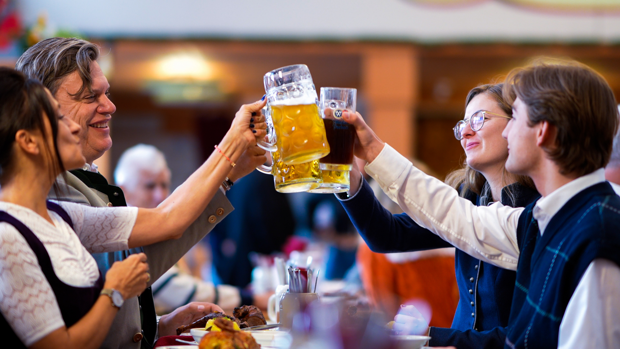 Vier Personen in Tracht stoßen mit Bierkrügen in einem Festzelt an Hühnerbraterei Poschner auf dem Oktoberfest